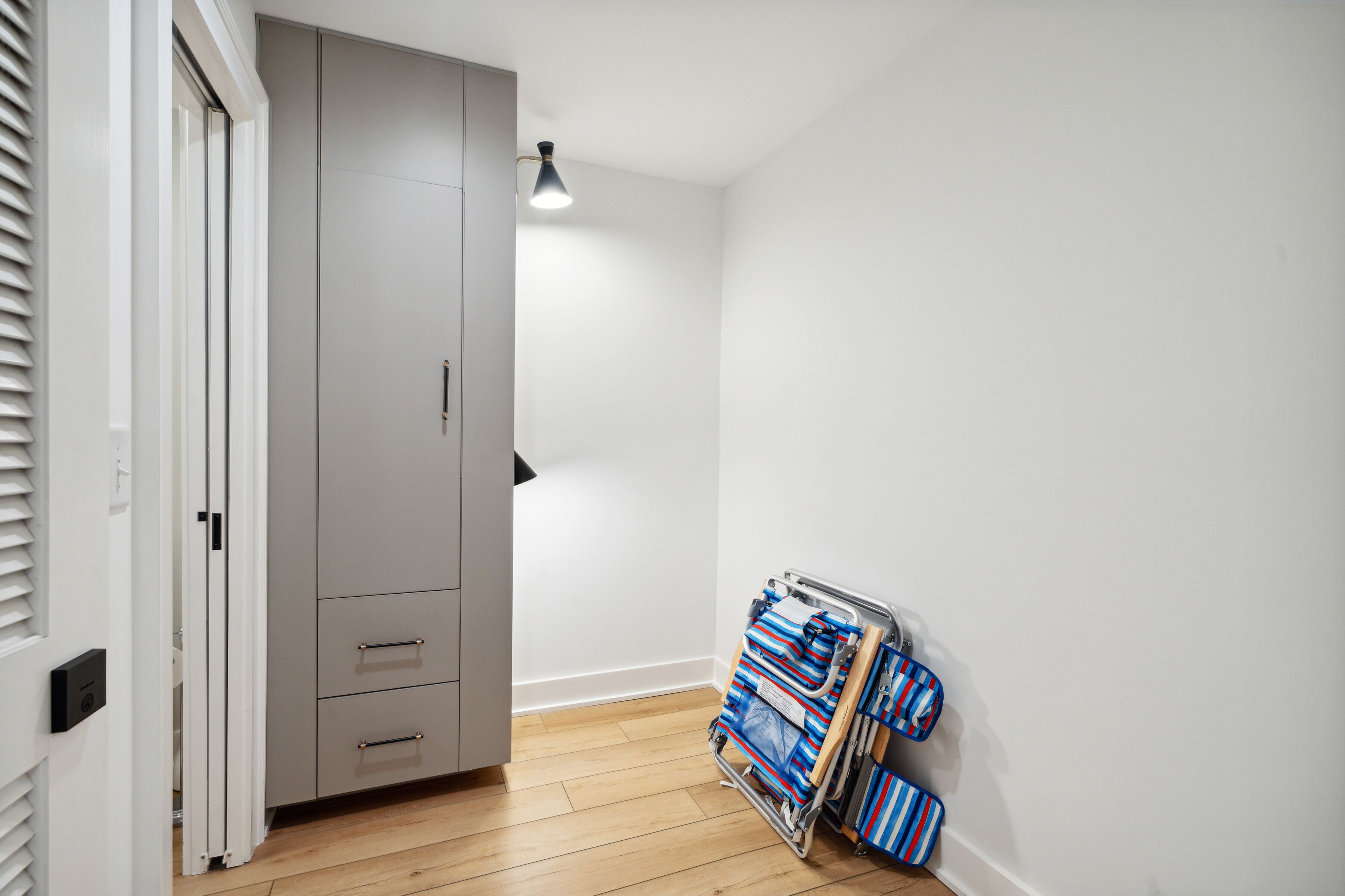 A room with a grey wardrobe, a metal rack with folded clothes, and a white wall.