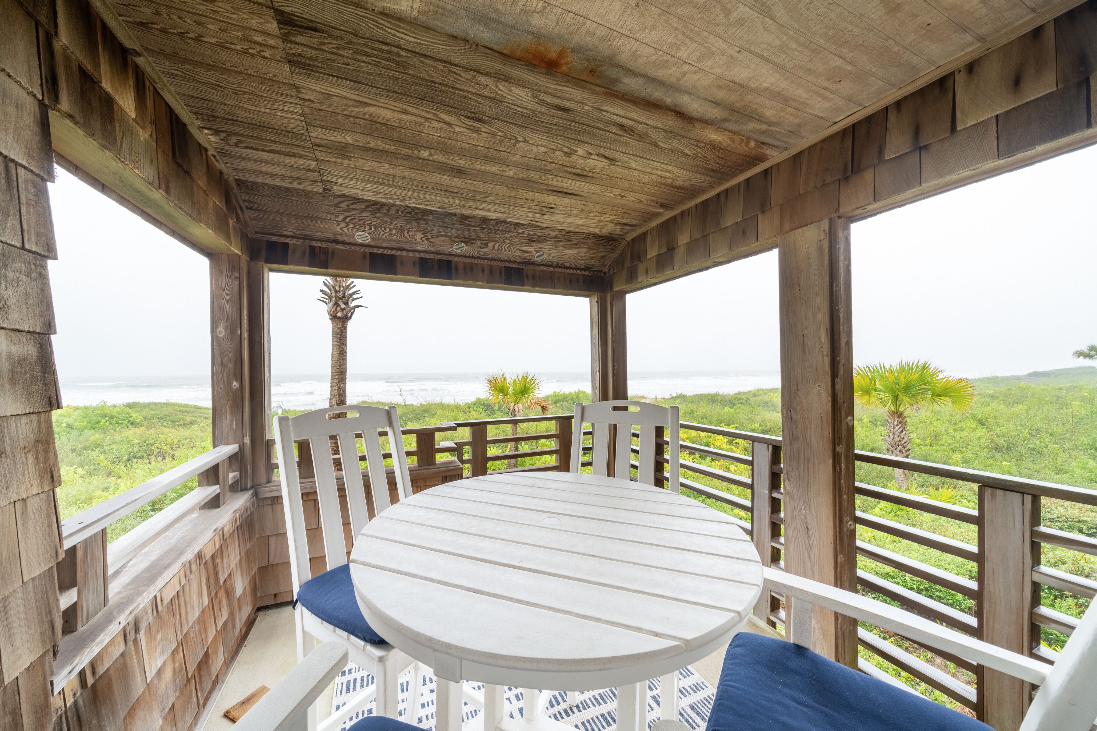 A wooden deck with a round table and chairs, overlooking a lush landscape.