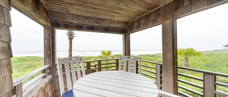 A wooden deck with a round table and chairs, overlooking a lush landscape.
