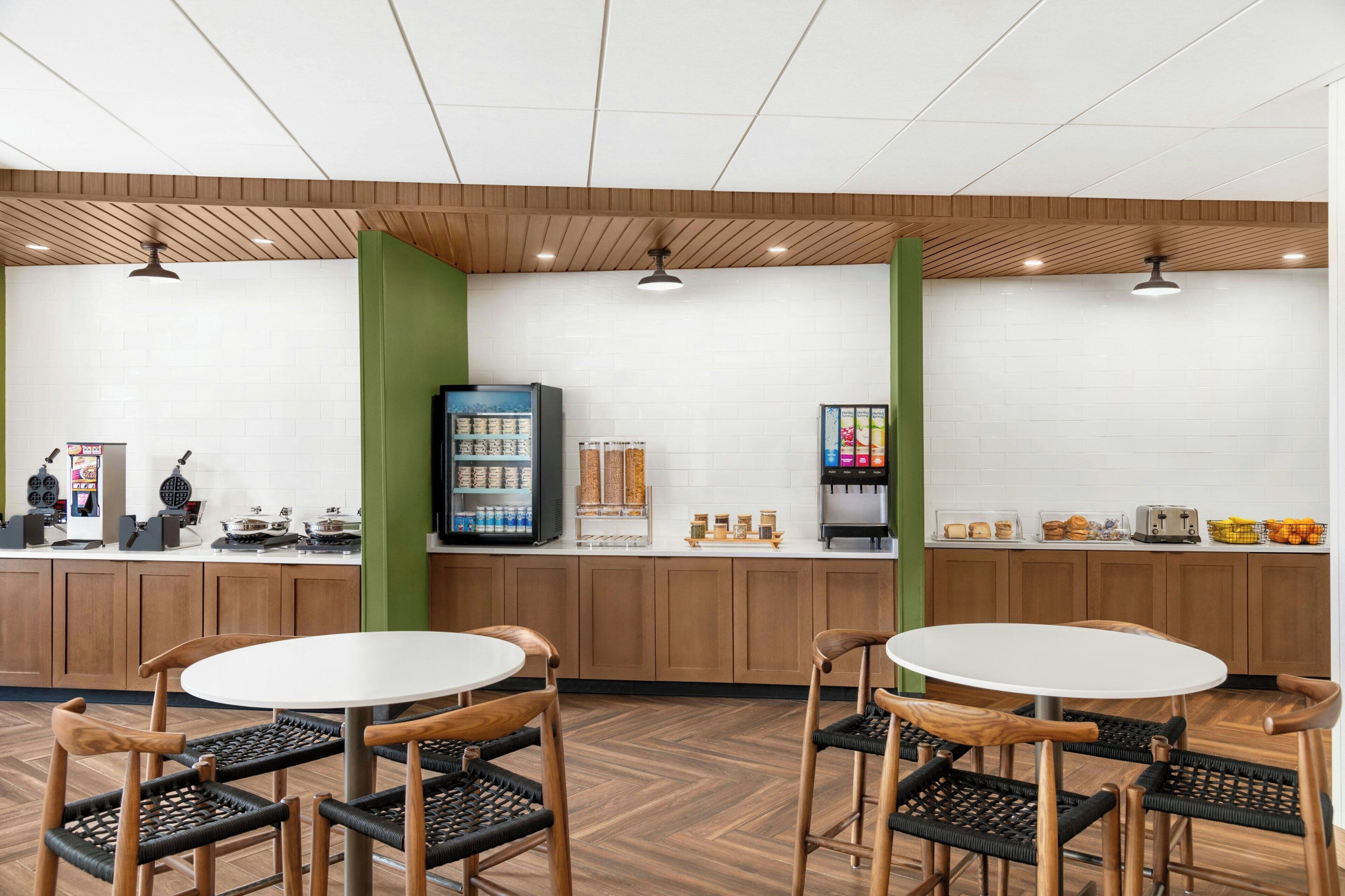 A cafe with wooden furniture, a white tiled wall, and a coffee machine.