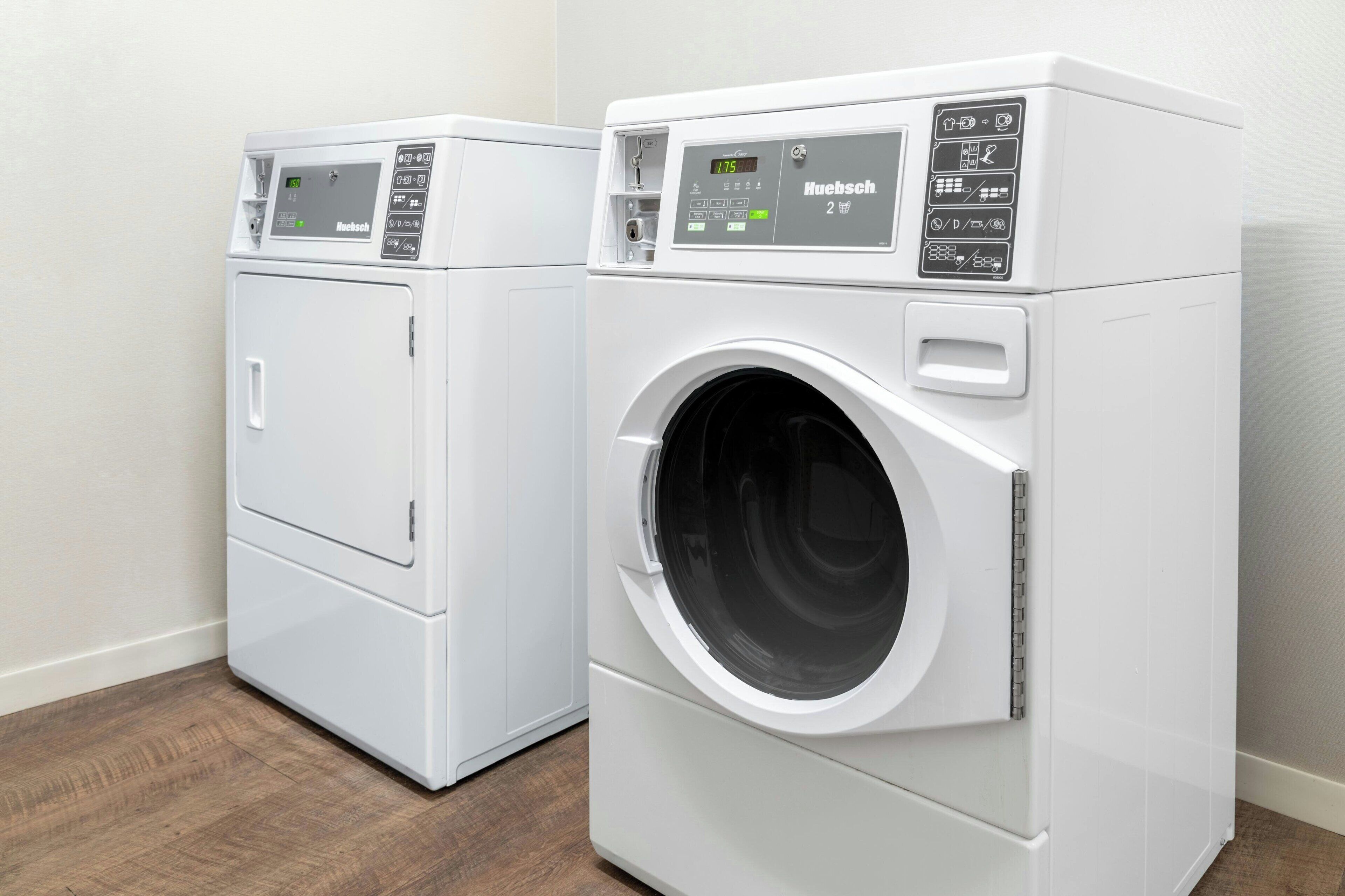 Two white front-loading washing machines in a corner of a room with wooden flooring.