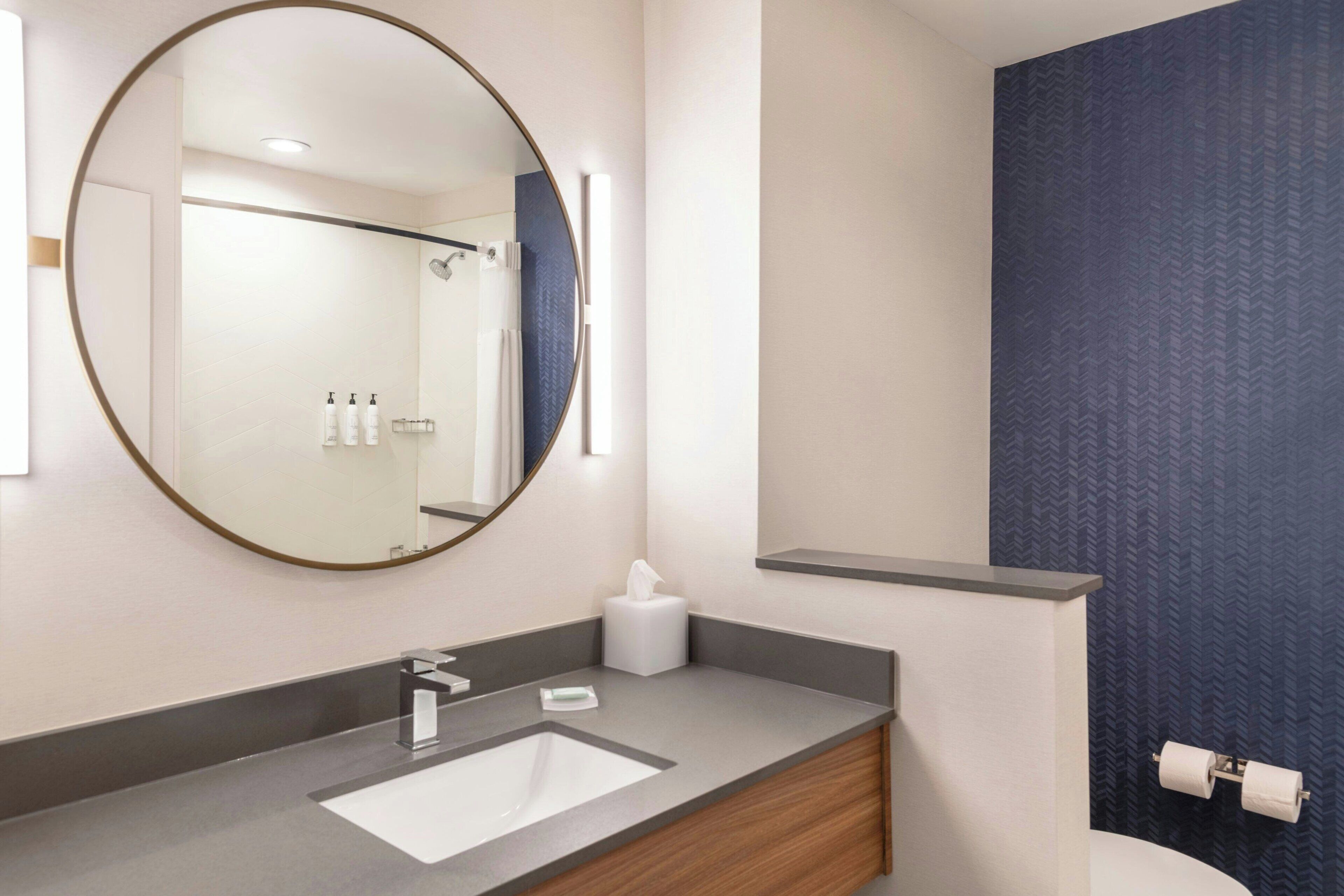 Une salle de bain moderne avec un miroir rond, un lavabo et des toilettes.