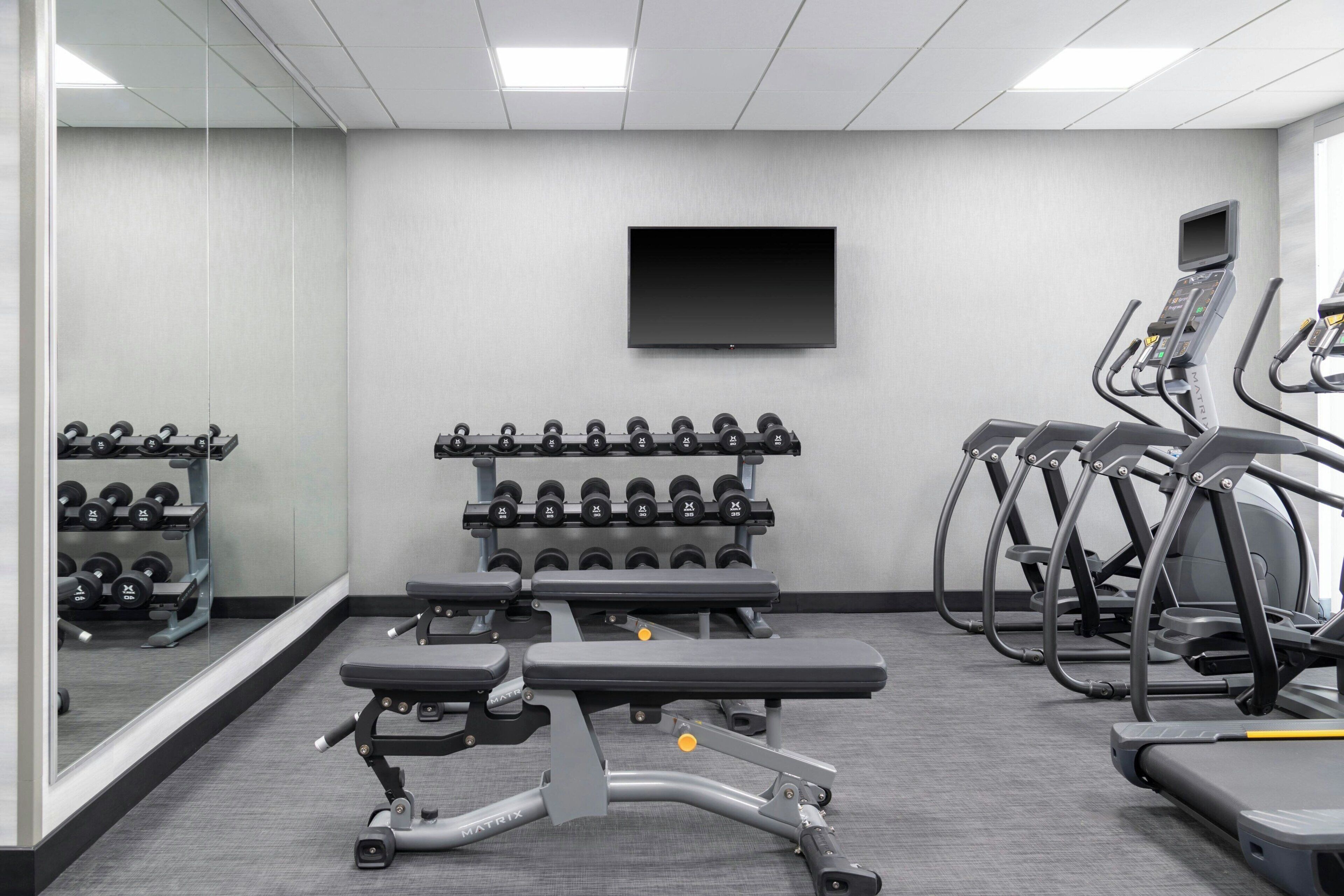 Un gimnasio con cintas de correr, mancuernas y un banco.