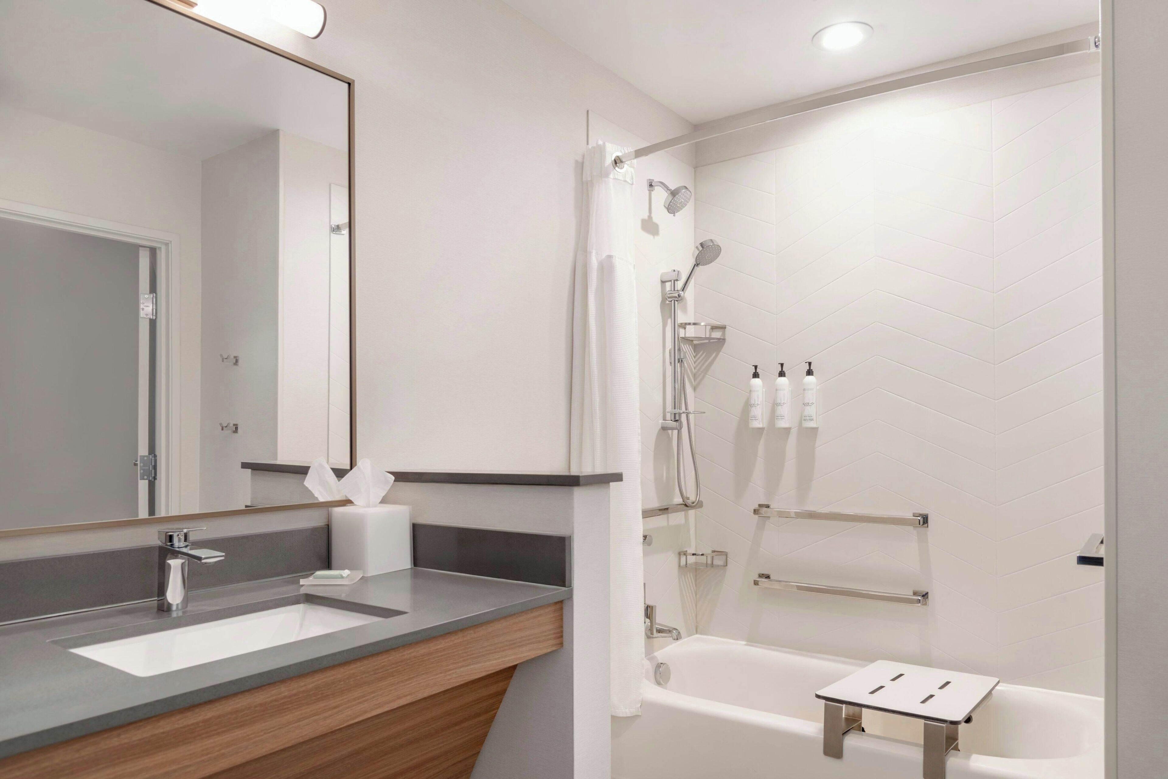 A modern bathroom with a large mirror, a sink, a shower with a handheld showerhead, and a small table.