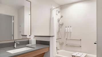 A modern bathroom with a large mirror, a sink, a shower with a handheld showerhead, and a small table.