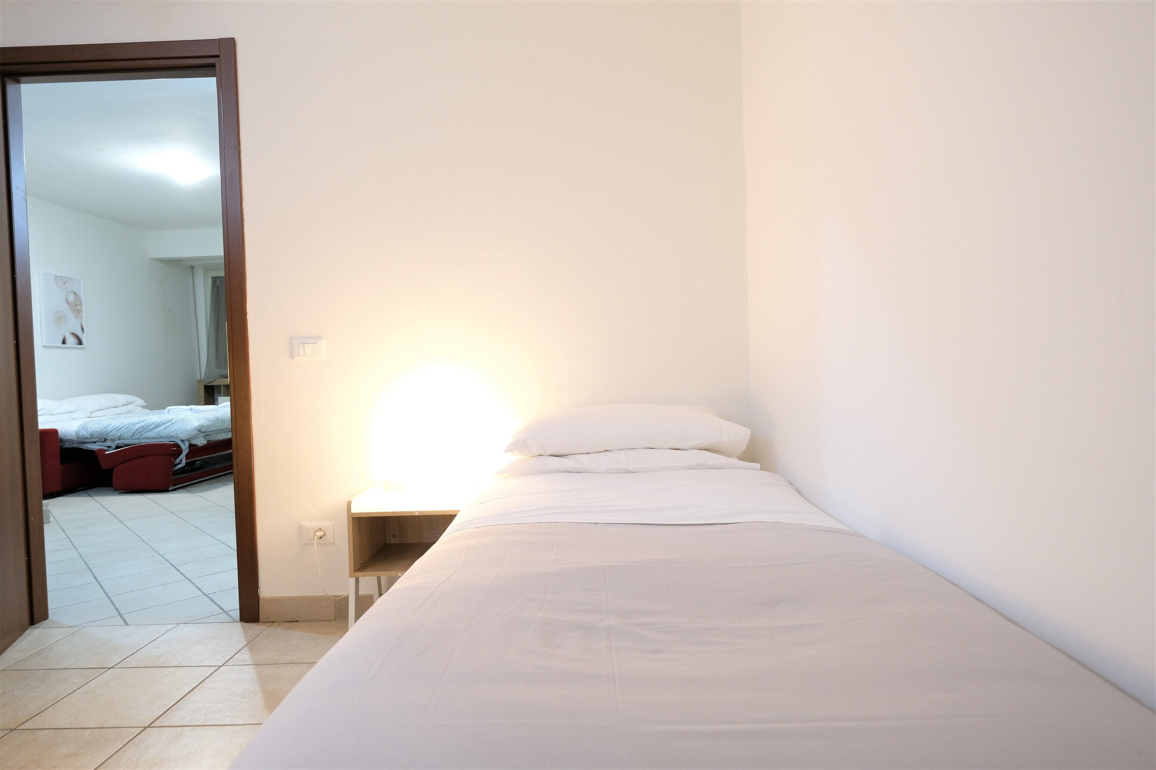 A small, neatly made bed in a room with white walls and a tiled floor.