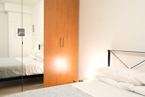 A bedroom with a wooden wardrobe, a bed with white bedding, and a bedside table. - Wine Apartments Florence Verdicchio  (Florence)