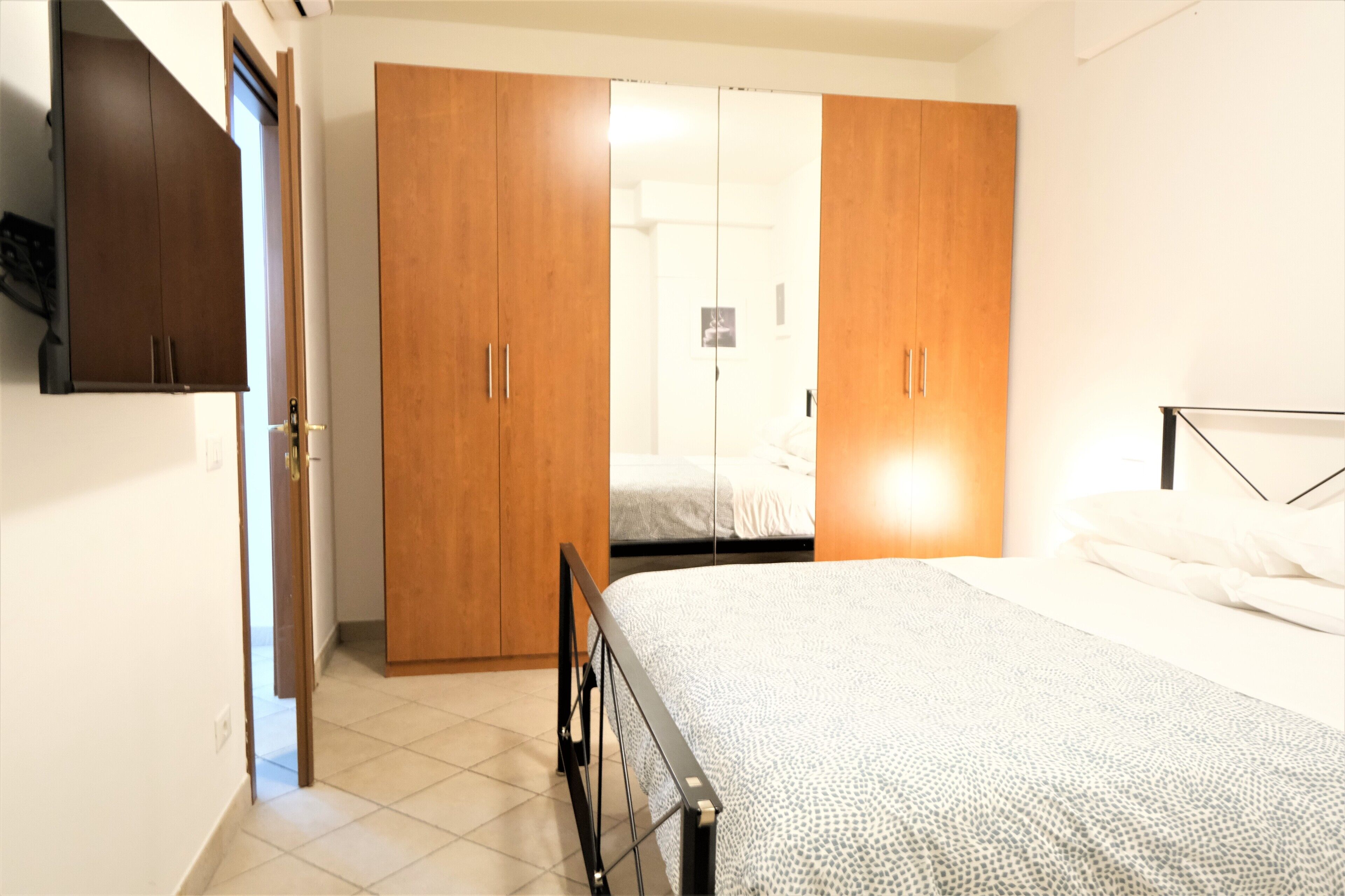 A bedroom with a bed, wooden wardrobe, and a door leading to another room.