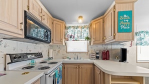 Une cuisine avec des meubles de rangement en bois, une cuisinière et une fenêtre ornée de rideaux à motifs floraux.