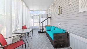 Une terrasse couverte avec une table et des chaises, un canapé avec des coussins et un escalier menant à un niveau supérieur.