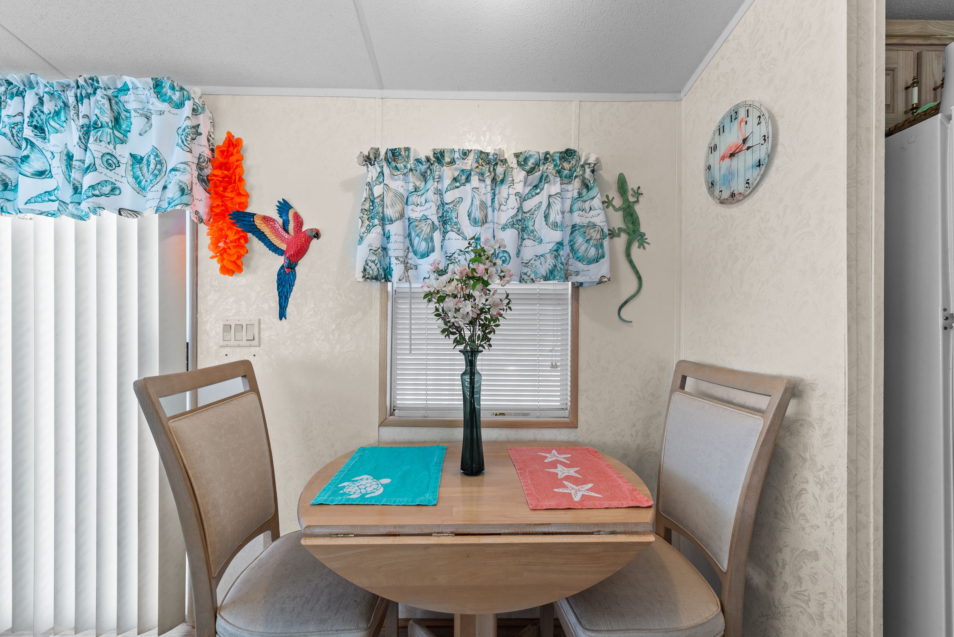 Un coin repas avec une table en bois, deux chaises, un vase de fleurs et des objets décoratifs accrochés au mur.