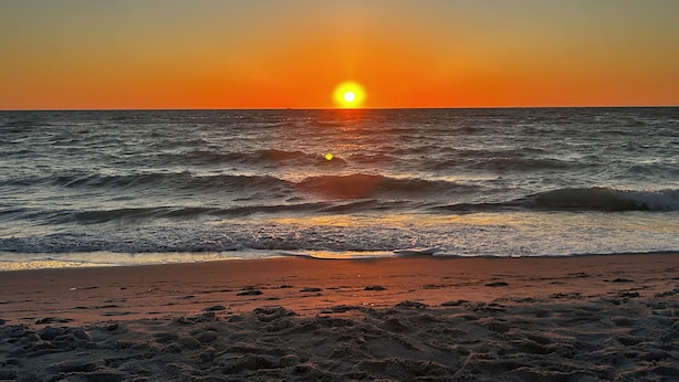 Un coucher de soleil sur l’océan, avec des vagues qui se rapprochent du rivage.