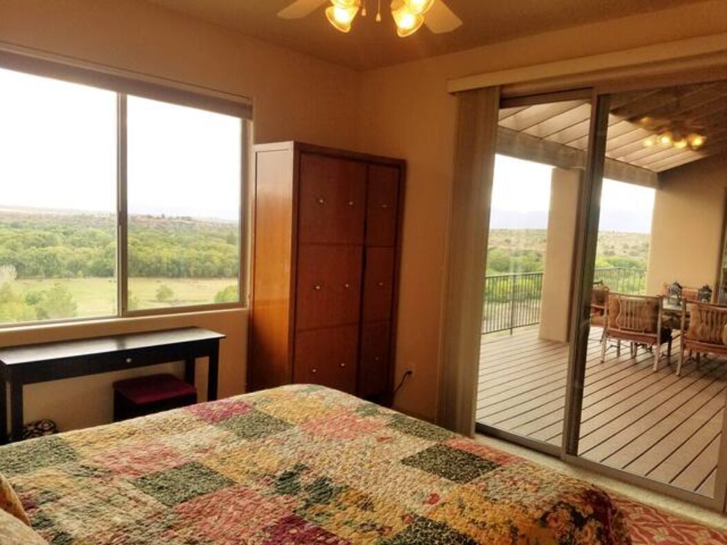 Une chambre dotée d’une grande fenêtre, d’une armoire en bois et d’un balcon aménagé avec du mobilier d’extérieur.