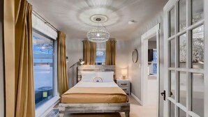 A hotel room with a bed, bedside table, lamp, and a view of the outdoors. - Olde Town Gold-3 bed/2 bath
 (Arvada)