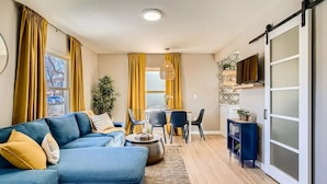 A modern living room with a blue sofa, yellow curtains, a dining area with chairs, and a sliding glass door. - Olde Town Gold-3 bed/2 bath
 (Arvada)