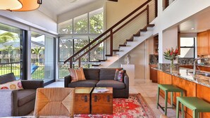 A spacious living area with a large sofa, a coffee table, and a rug. There is a staircase leading to an upper level, and a kitchen area with a marble countertop. - Snorkel with sea turtles! Ocean Front & Pool! (Lahaina)