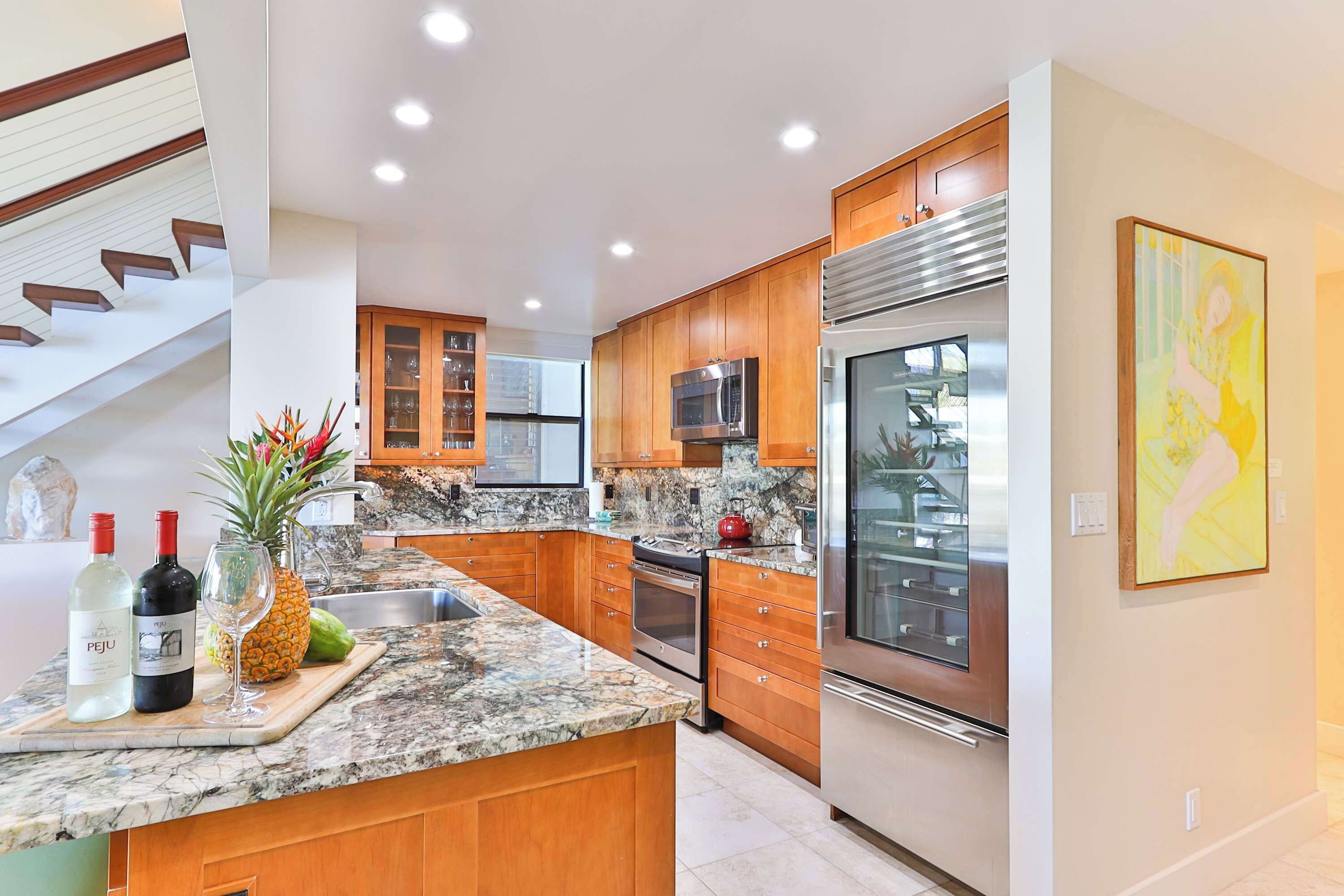 A modern kitchen with wooden cabinets, granite countertops, stainless steel appliances, and a central island with a fruit bowl.