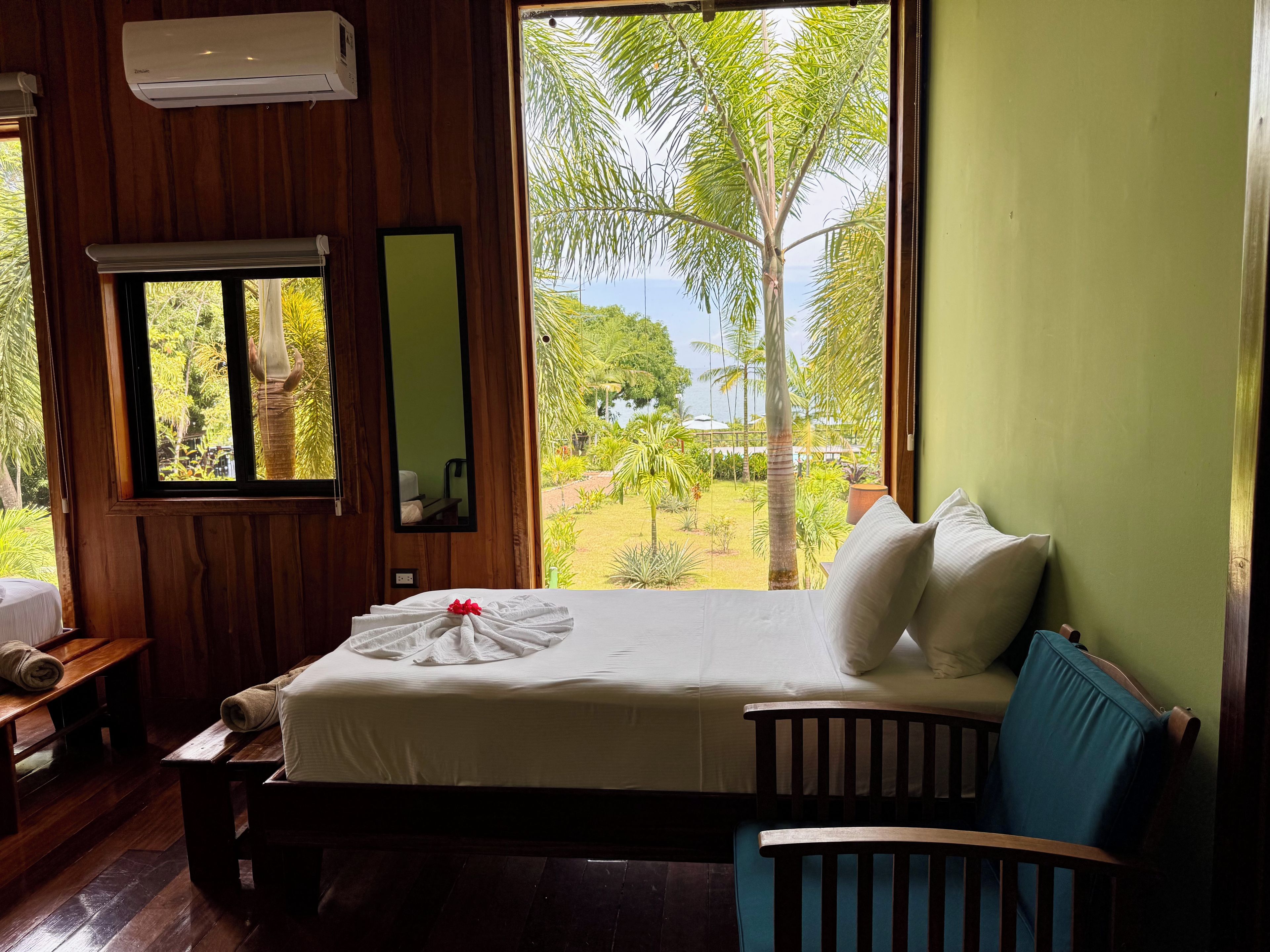 Una habitación con cama, un banco, una ventana y vistas a un jardín y al agua.