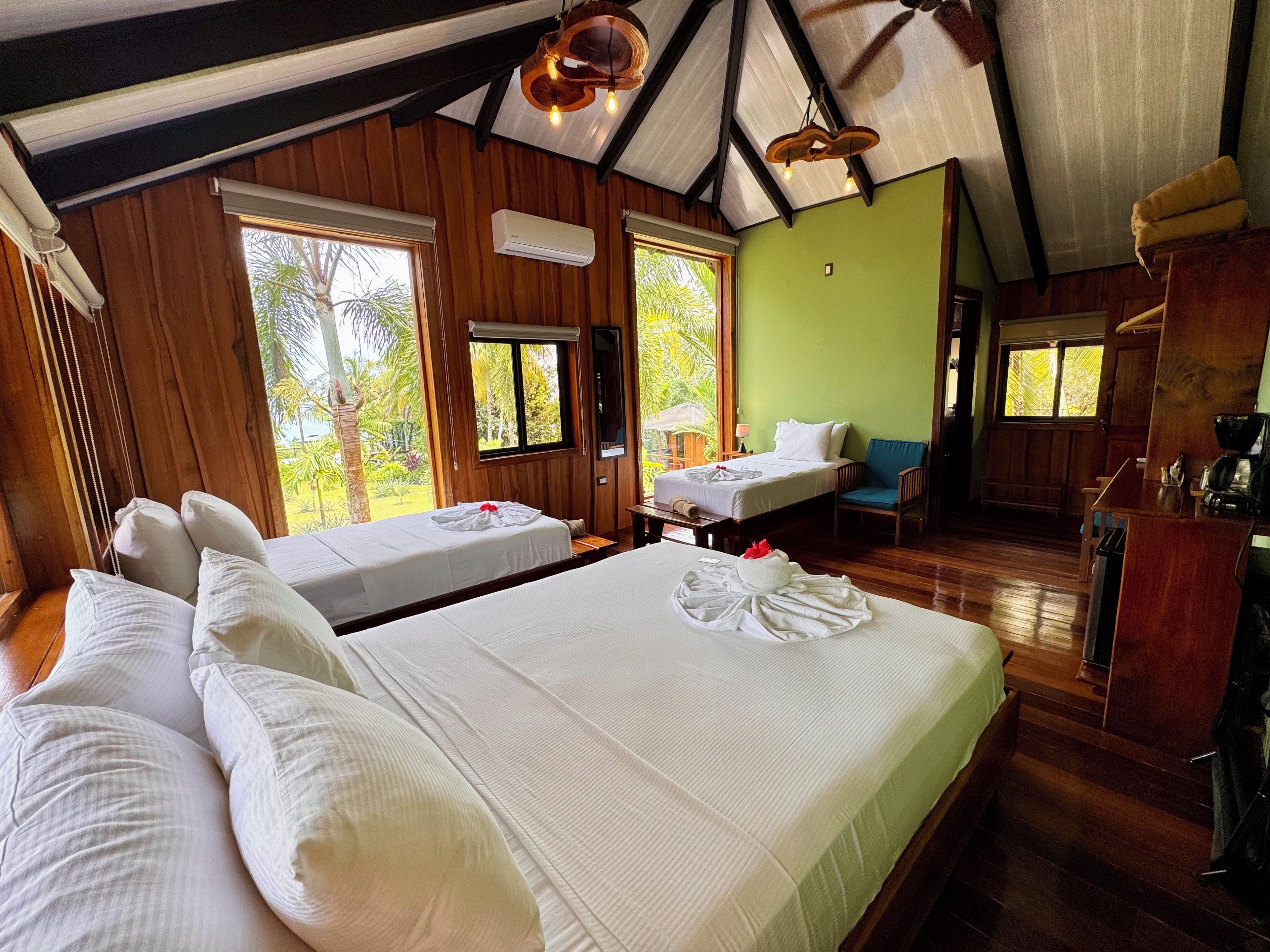 A hotel room with two beds, a wooden ceiling, and large windows.