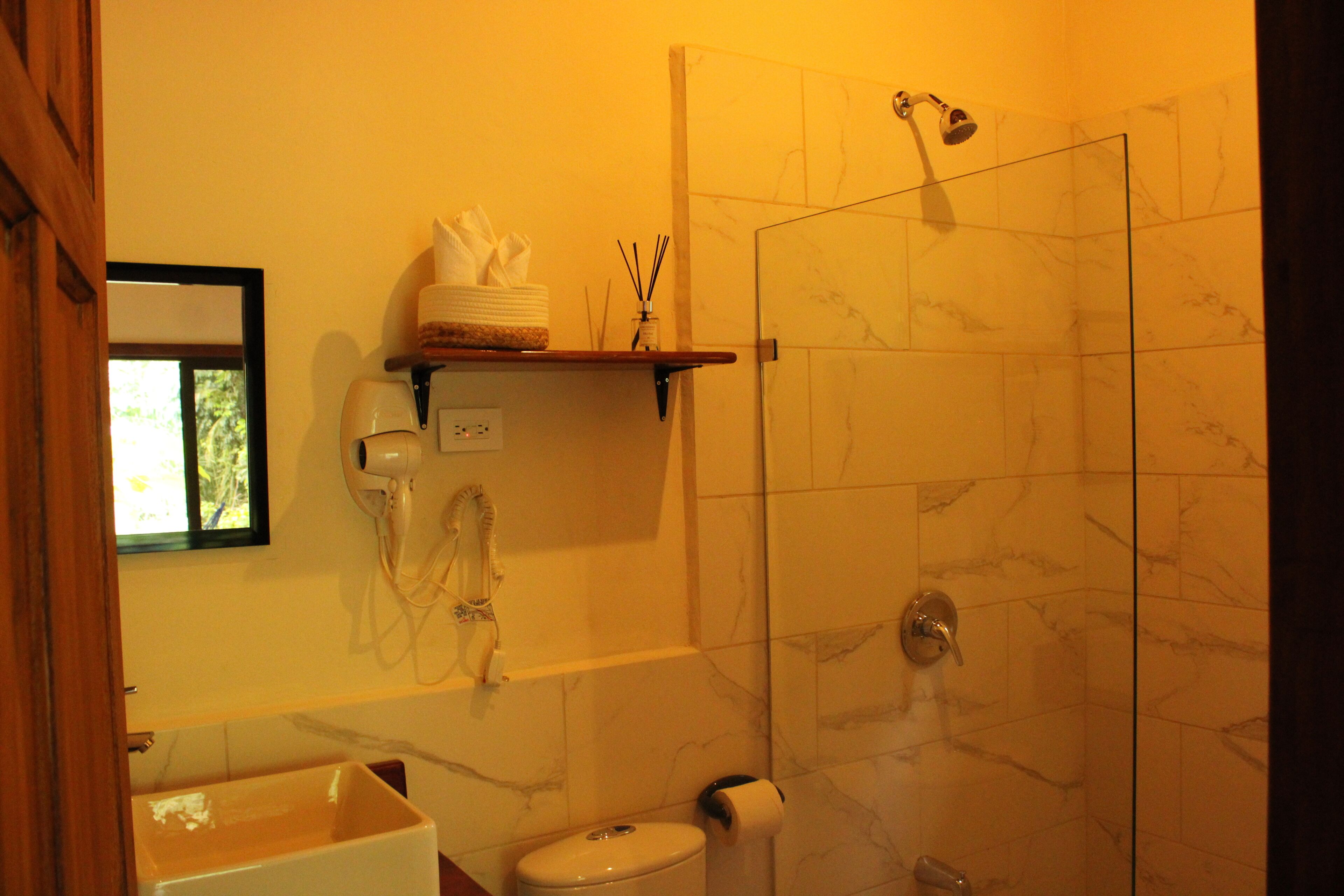A bathroom with a shower, toilet, and a shelf with toiletries.