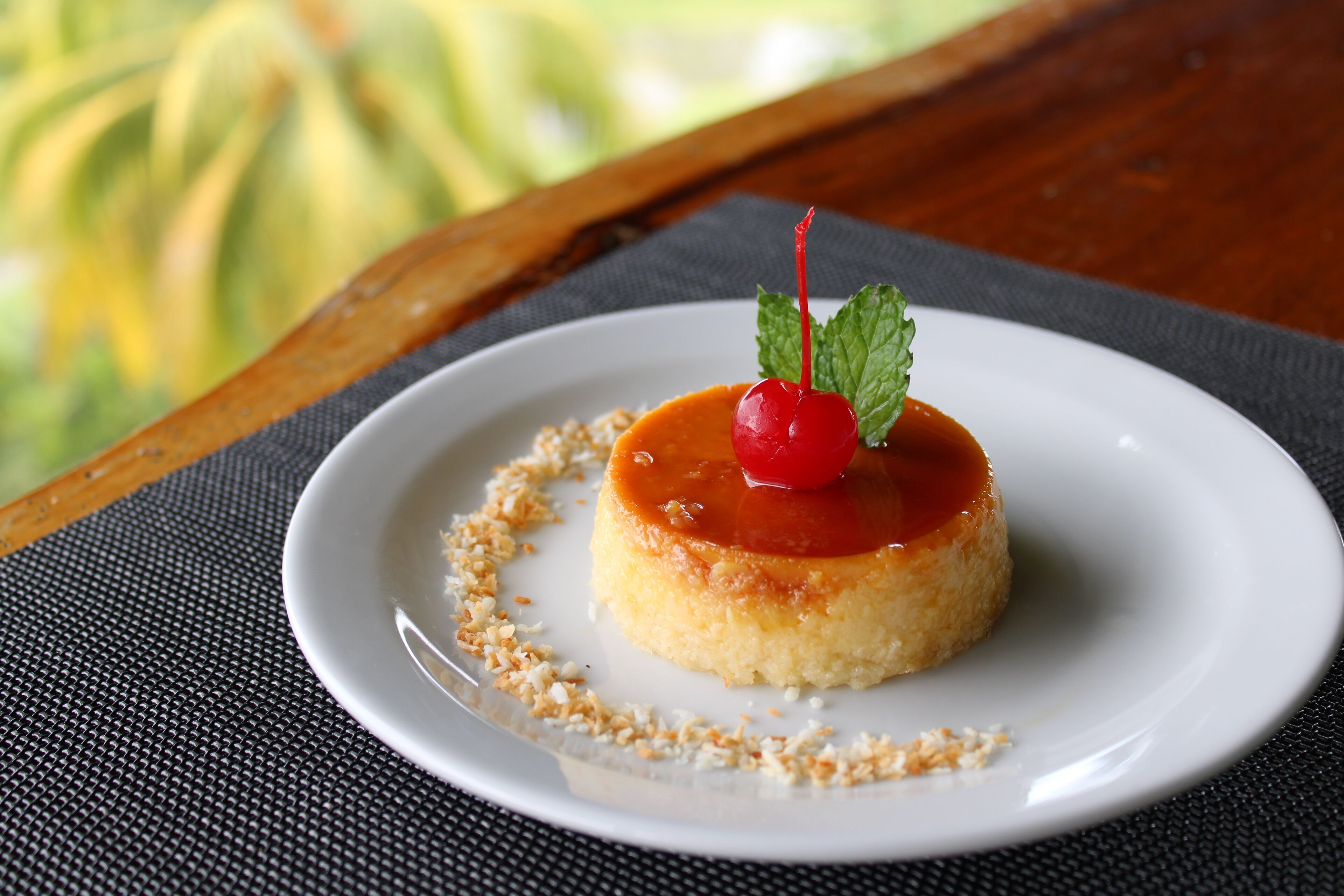 Ein Dessert auf einem weißen Teller, mit einer Kirsche darauf, platziert auf einer strukturierten Unterlage.