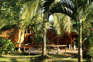 A wooden building with a covered outdoor seating area surrounded by palm trees. - Natural Drake Bay Hotel Boutique (Drake Bay)