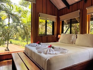 A bed with white bedding and a red flower, wooden walls, and a view of greenery outside. - Natural Drake Bay Hotel Boutique (Drake Bay)