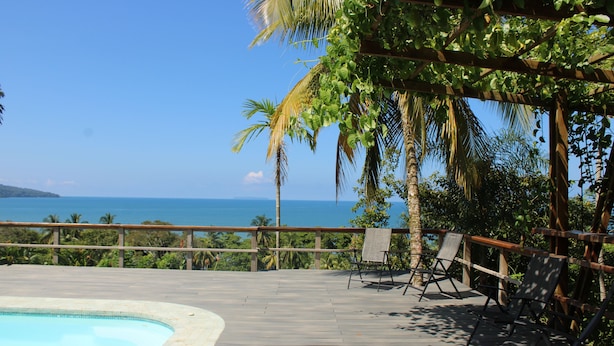Un terrazzo in legno con piscina, sedie a sdraio e vista sull'oceano.