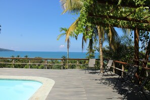 A wooden deck with a pool, lounge chairs, and a view of the ocean. - Natural Drake Bay Hotel Boutique (Drake Bay)