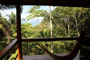 Una hamaca en una terraza de madera con vistas a un exuberante bosque tropical y el océano.