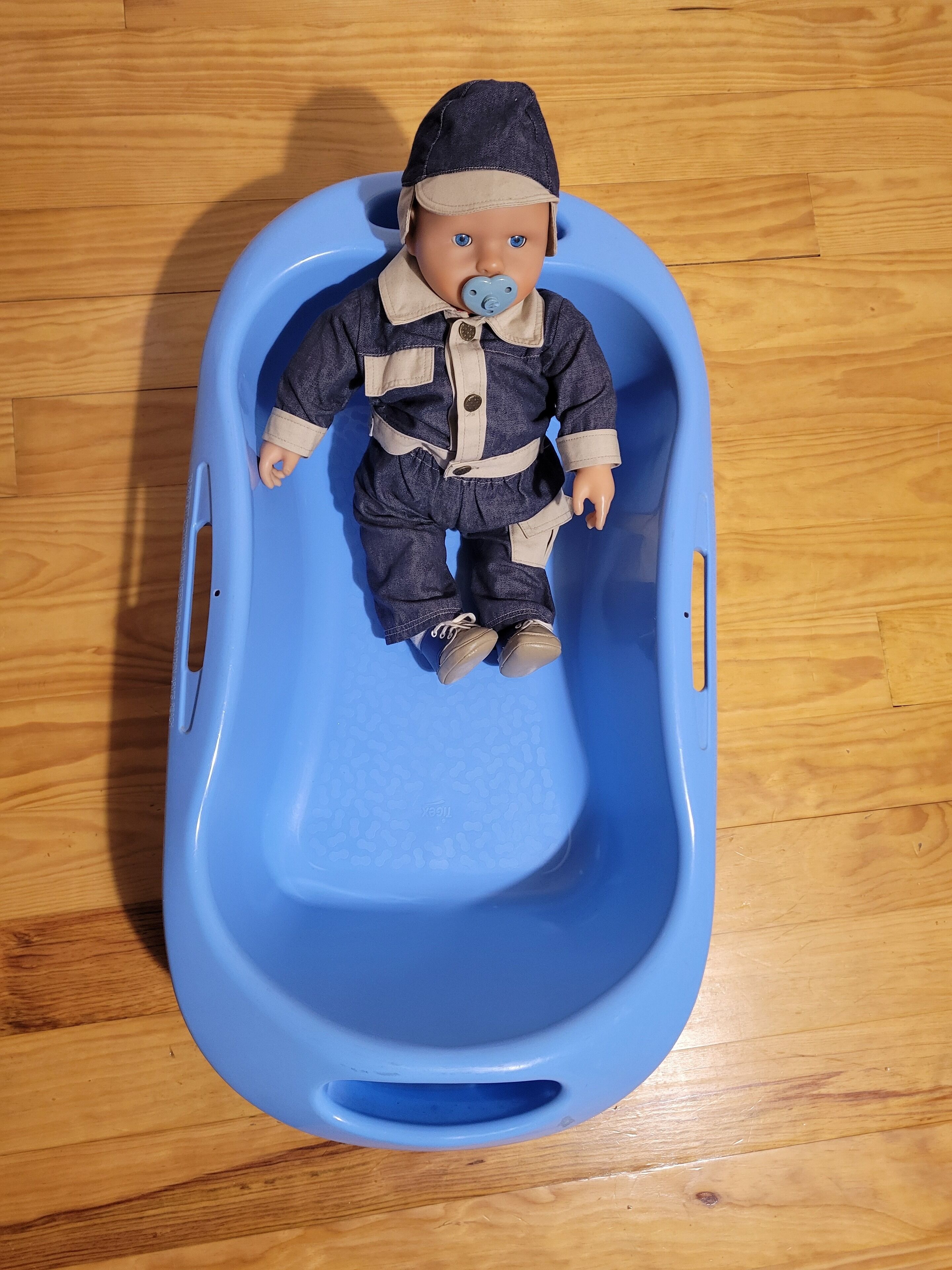 A doll in a blue plastic tub.
