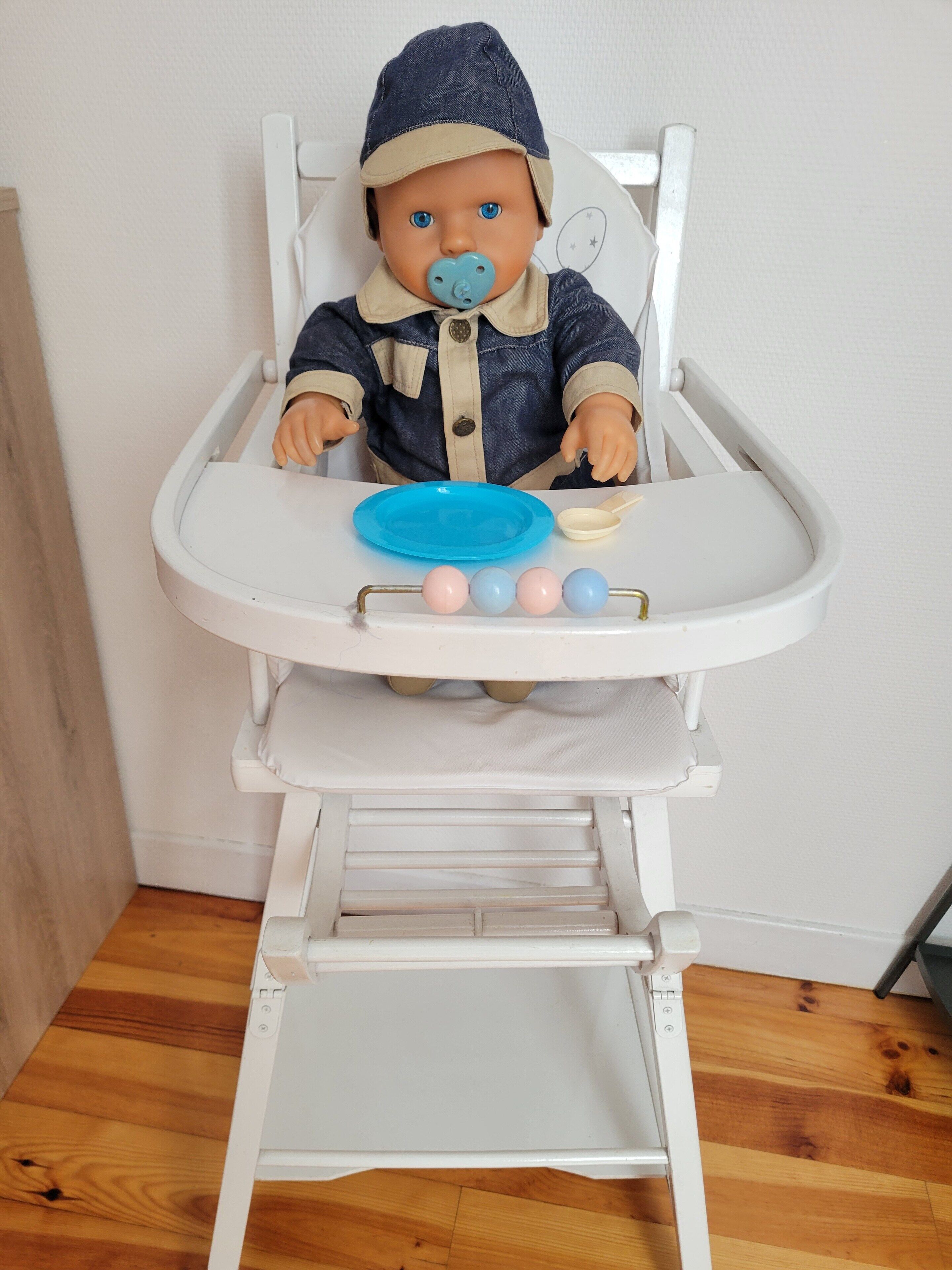 A baby in a high chair with a blue plate and a spoon.