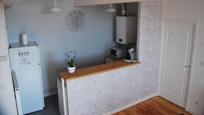 A compact kitchen with a white brick wall, a wooden countertop, a white refrigerator, a clock, and a white door. - Château des Princes " Fleur de Lys " (Sedan)