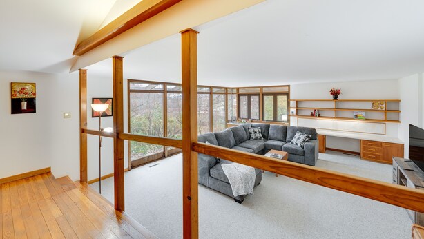 A spacious living area with a wooden ceiling, a gray sectional sofa, a wooden desk, and a large window offering a view of the outdoors. - Historic Wisconsin Retreat on 26-Acre Property! (Plain)