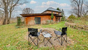 A house with a brick exterior and a metal roof, surrounded by a grassy yard with two black folding chairs and a small fire pit. - Historic Wisconsin Retreat on 26-Acre Property! (Plain)