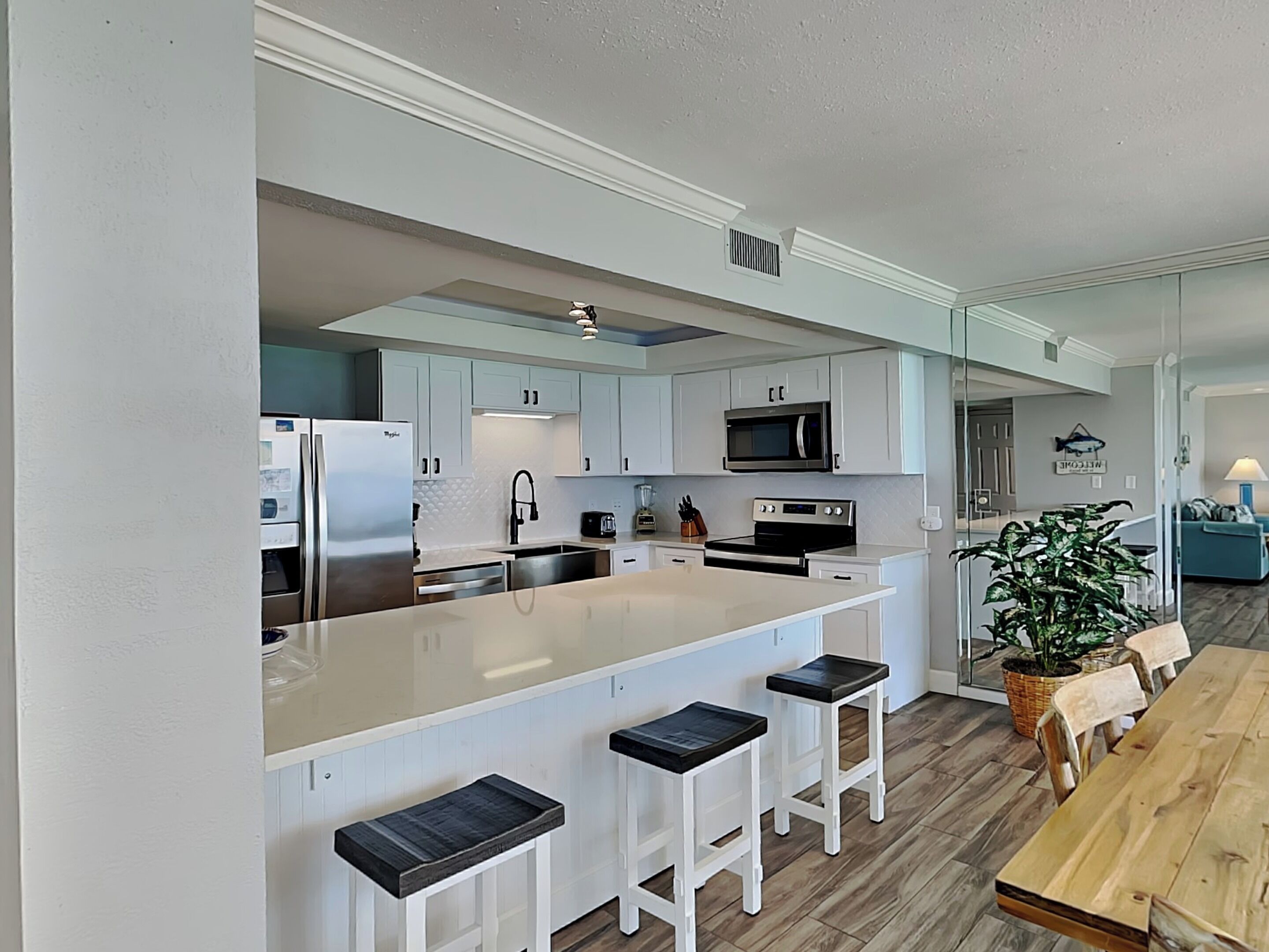A modern kitchen with white cabinets, a large island with bar stools, a microwave, and an oven.