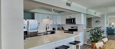 A modern kitchen with white cabinets, a large island with bar stools, a microwave, and an oven.