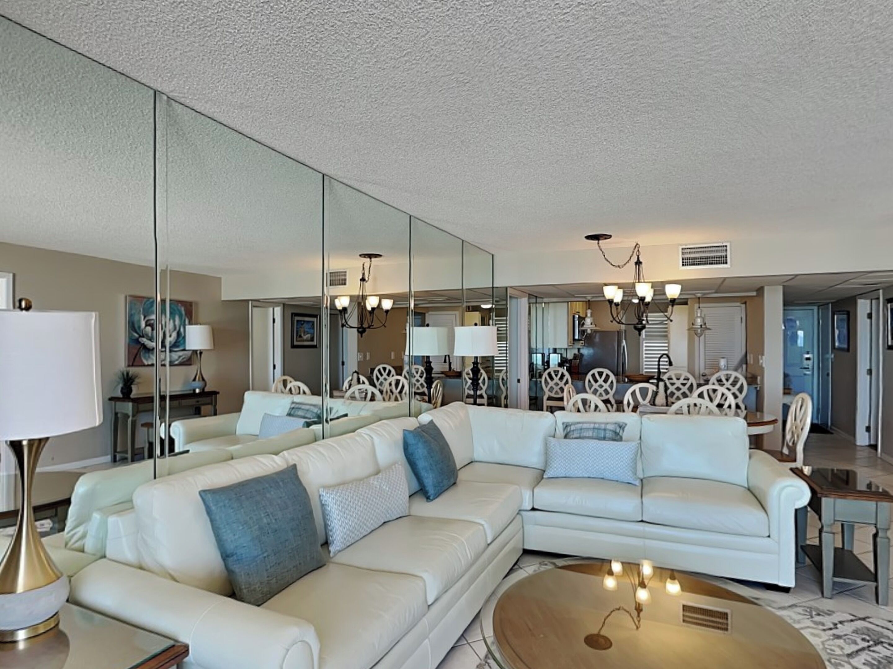 A modern living room with a sectional sofa, a round coffee table, and a dining area with white chairs and a chandelier.
