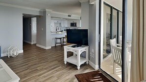 Un appartement moderne doté d’une cuisine, d’un espace de vie avec télévision et d’une porte-fenêtre coulissante donnant sur un balcon.