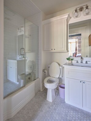 A bathroom with a glass-enclosed shower, a toilet, a sink with a mirror, and a vanity with cabinets.