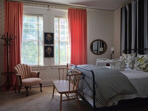 A bedroom with a bed, a chair, a table, and a window with curtains.