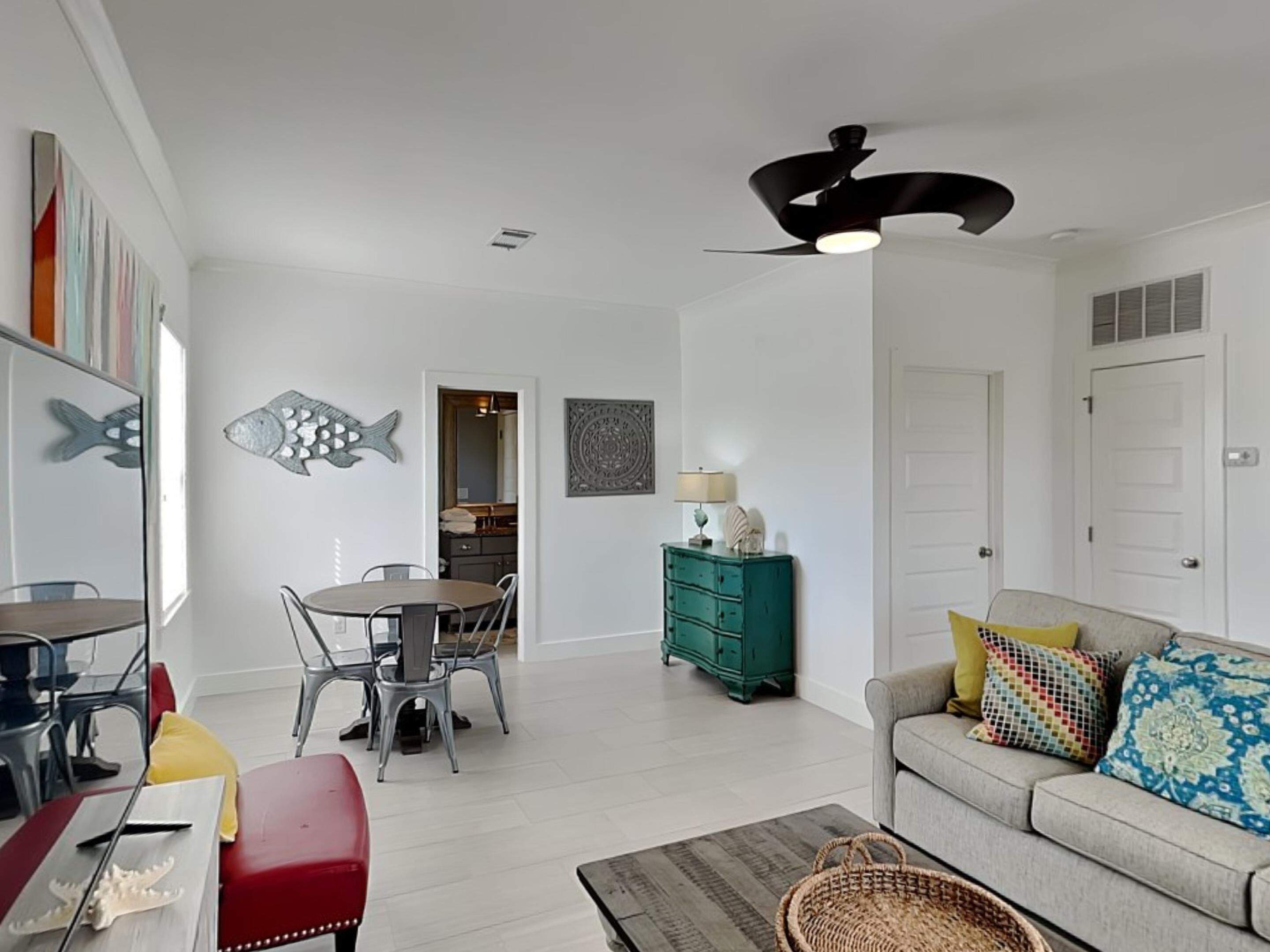A modern living room with a dining area, a teal dresser, and a gray sofa with colorful cushions.