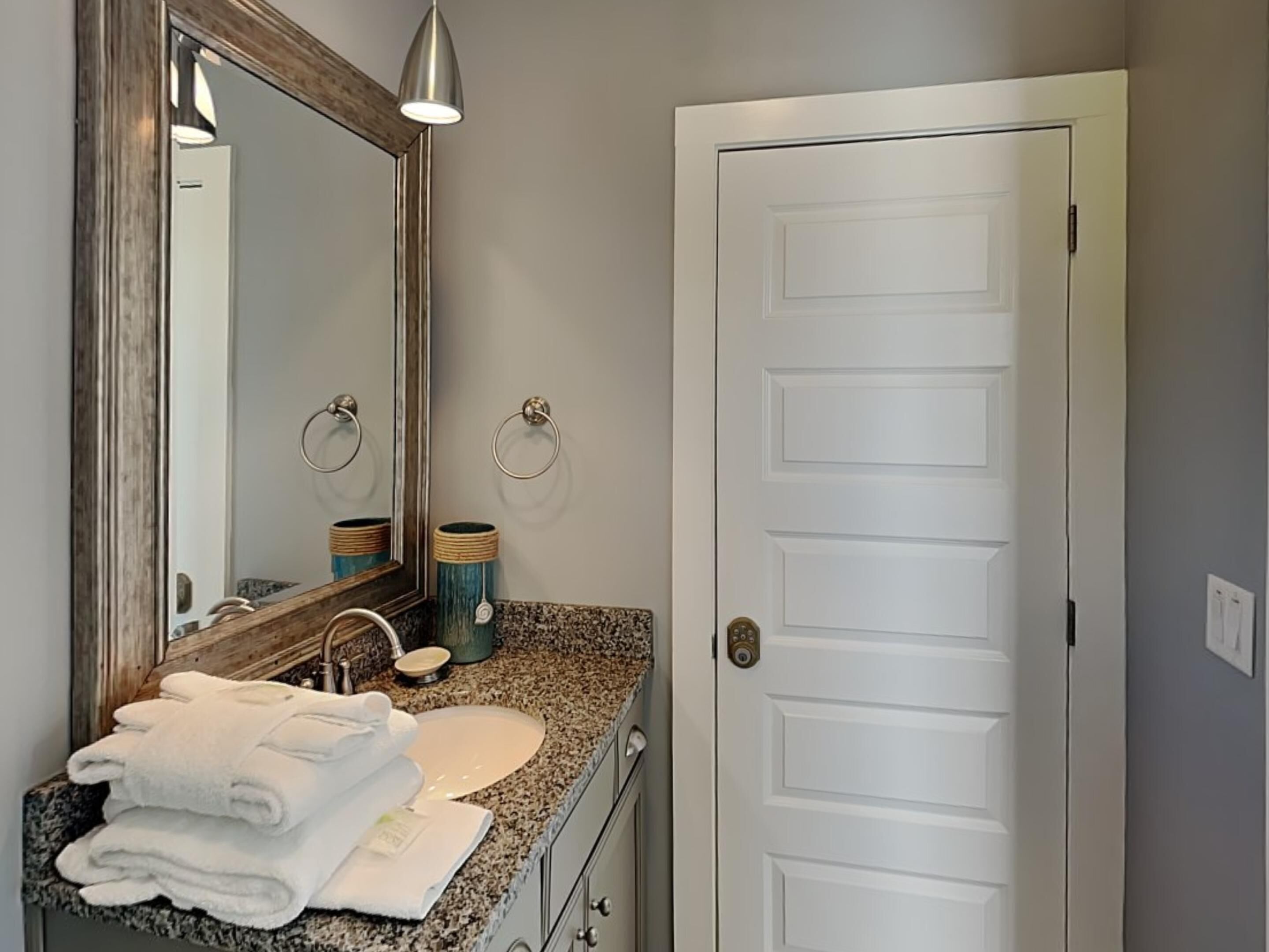 A bathroom with a granite countertop, a sink, a mirror, a towel rack, and a door.