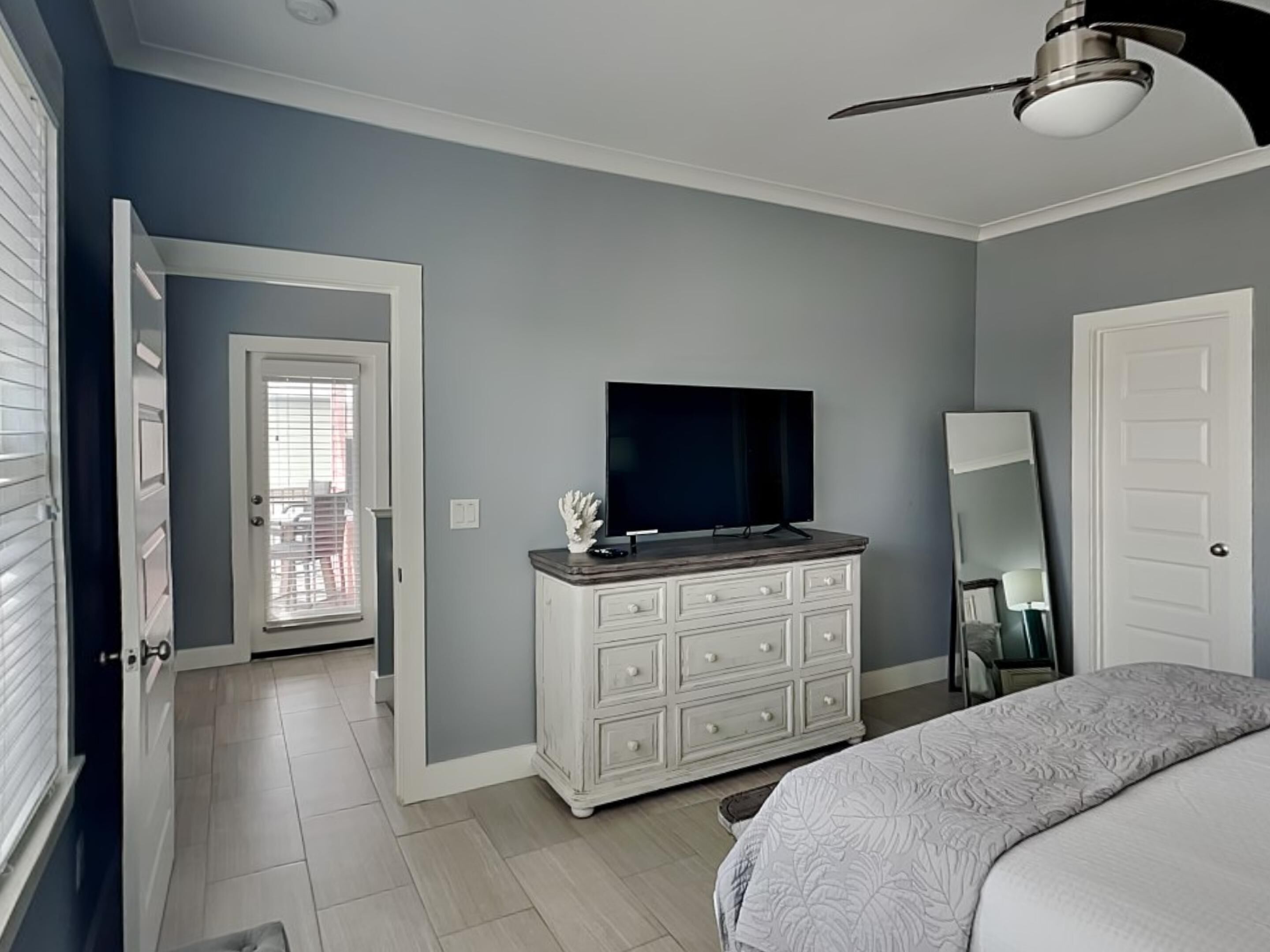 Une chambre à coucher comprenant un lit, une commode, un téléviseur et un ventilateur de plafond.