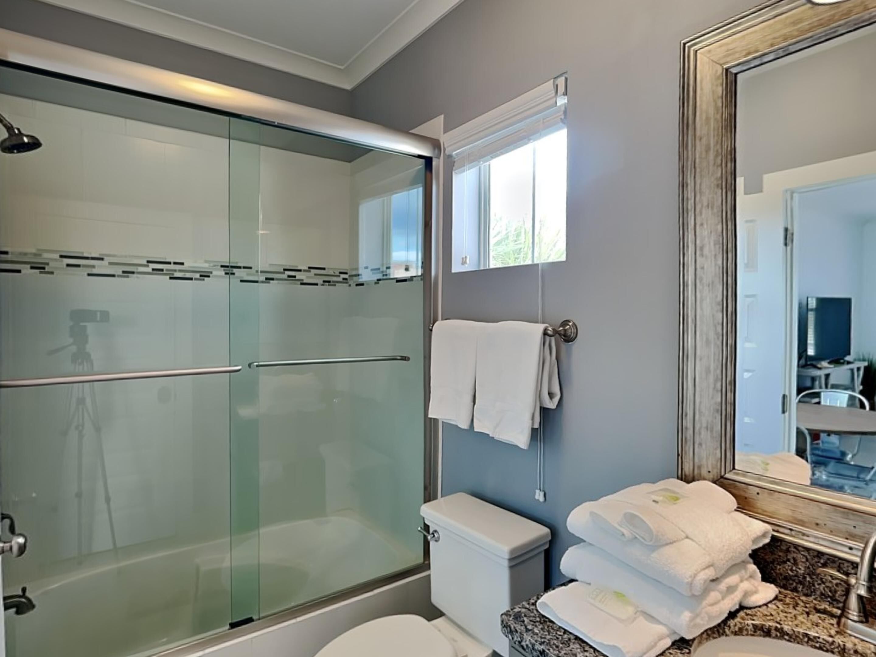 A modern bathroom with a glass-enclosed shower, a toilet, and a sink with stacked towels.