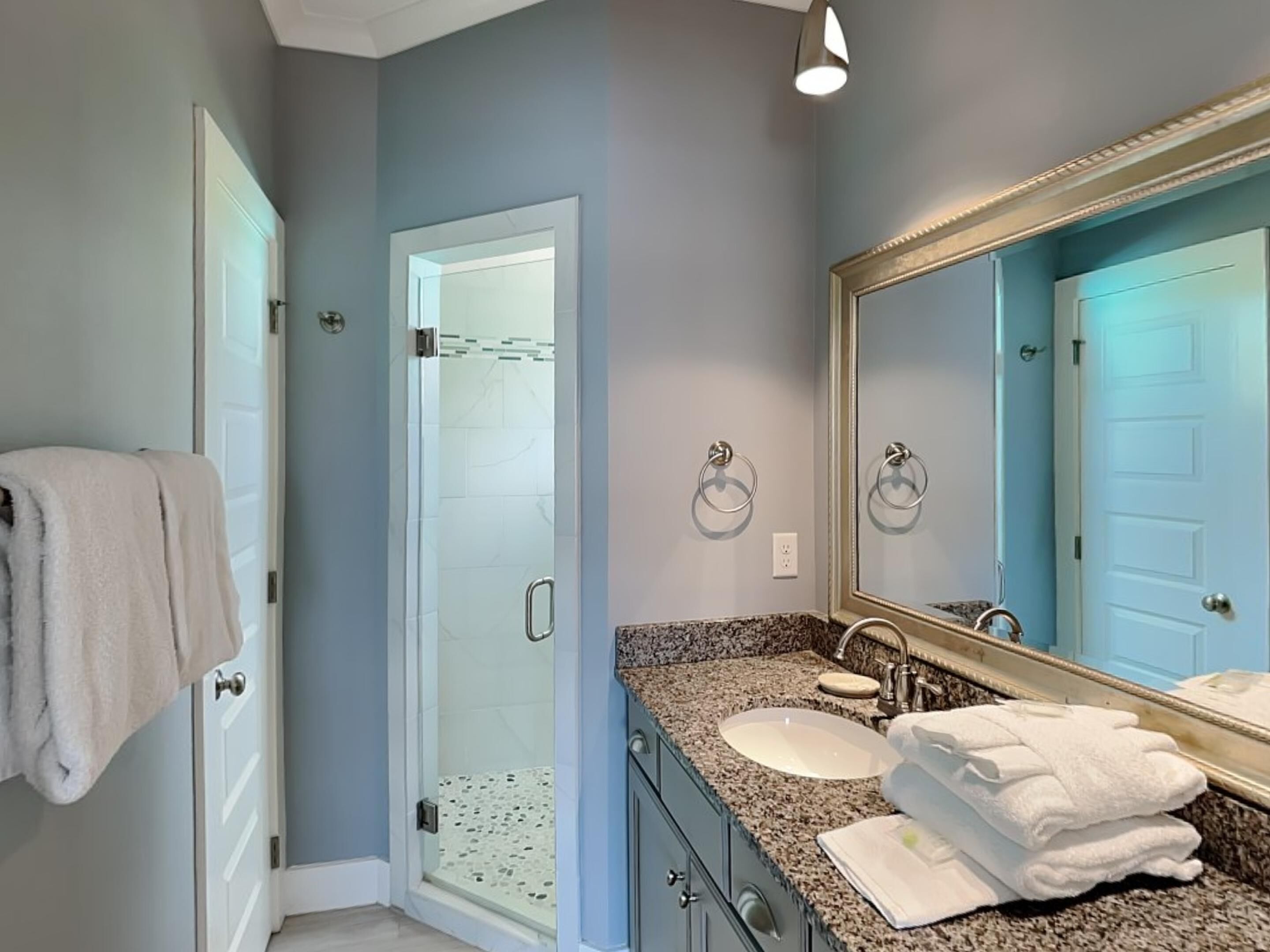 Un baño con mampara de vidrio, lavamanos con tocador y un espejo grande.