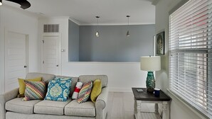 A living room with a grey sofa, colorful cushions, a small table with a lamp, and a window with blinds. - Runnin Down A Dream by Southern Vacation Rentals (Miramar Beach)