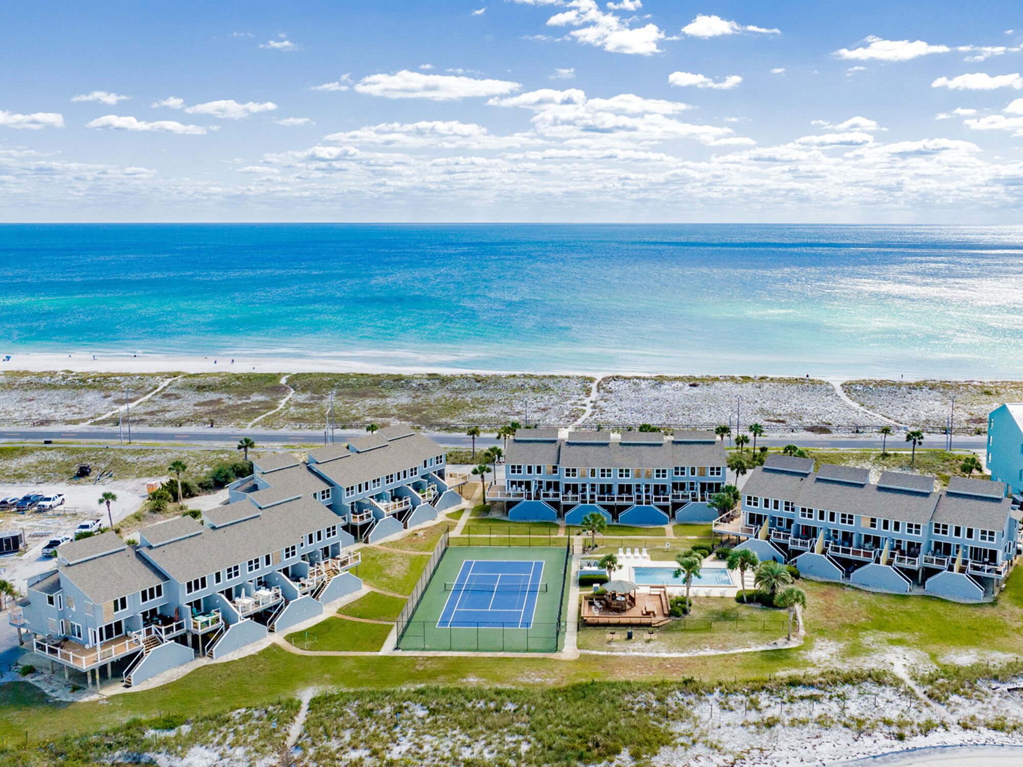A coastal hotel with multiple buildings, a tennis court, and a beach view.