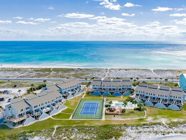 A coastal hotel with multiple buildings, a tennis court, and a beach view.