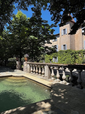 A stone bridge over a clear water feature, with a building in the background.